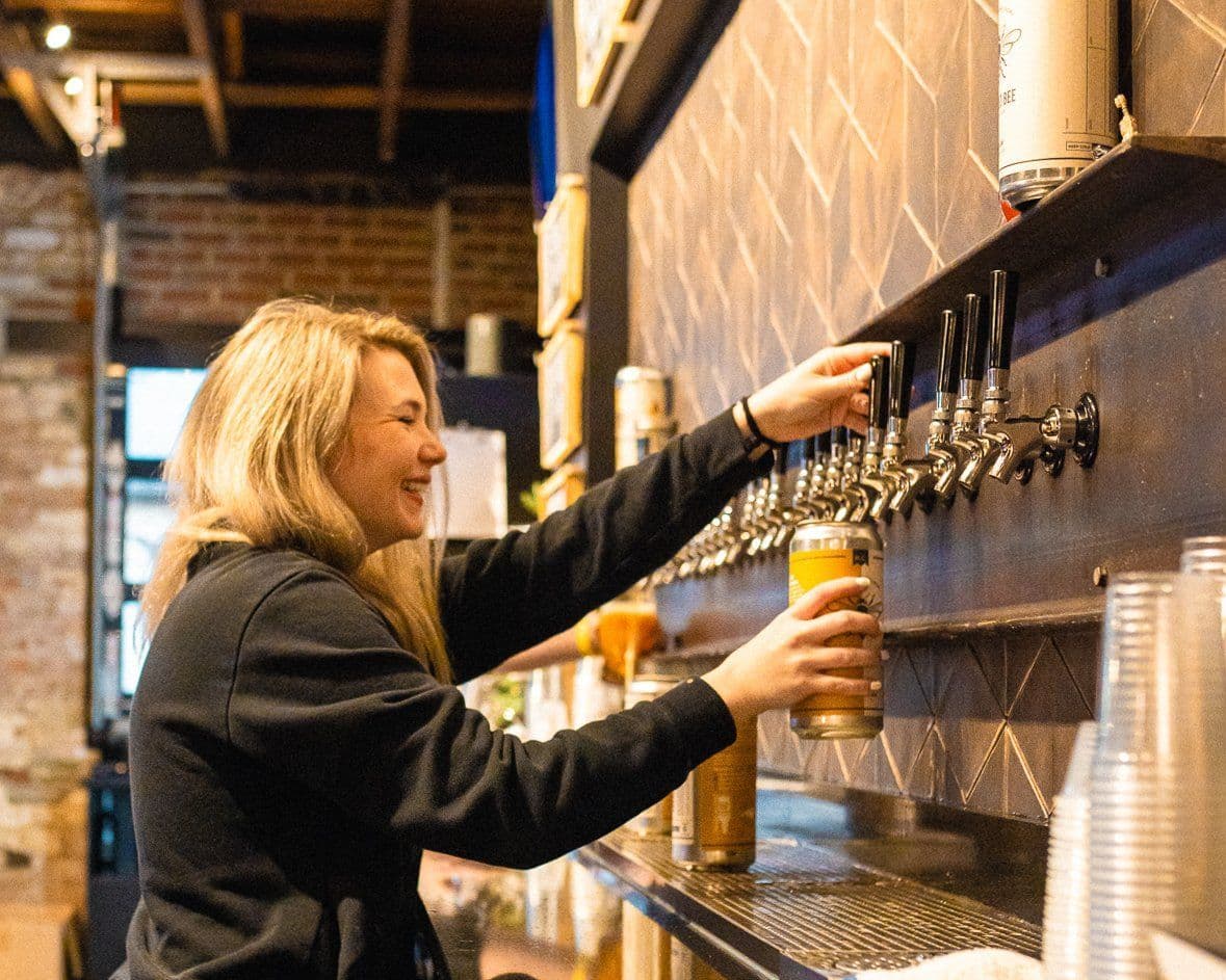 A smiling Bearded Bee team member pouring a beer at the taproom
